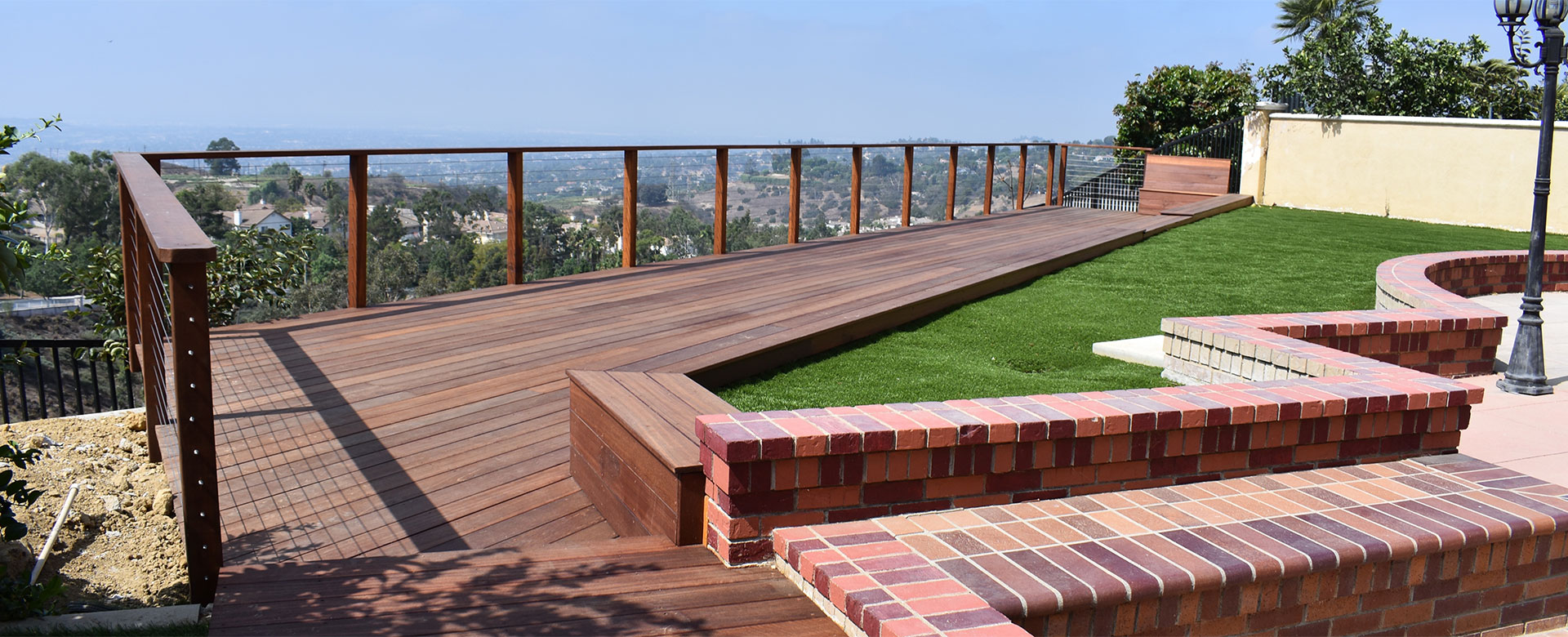 wooden deck with grass and brick overlooking a sunny city