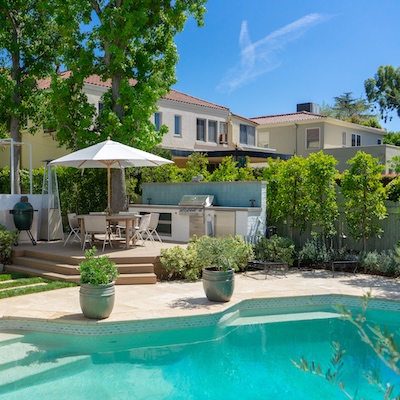 Raised deck with seating and BBQ in the backyard by a pristine pool