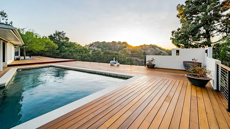 A wooden deck surrounding a pool overlooking green mountains