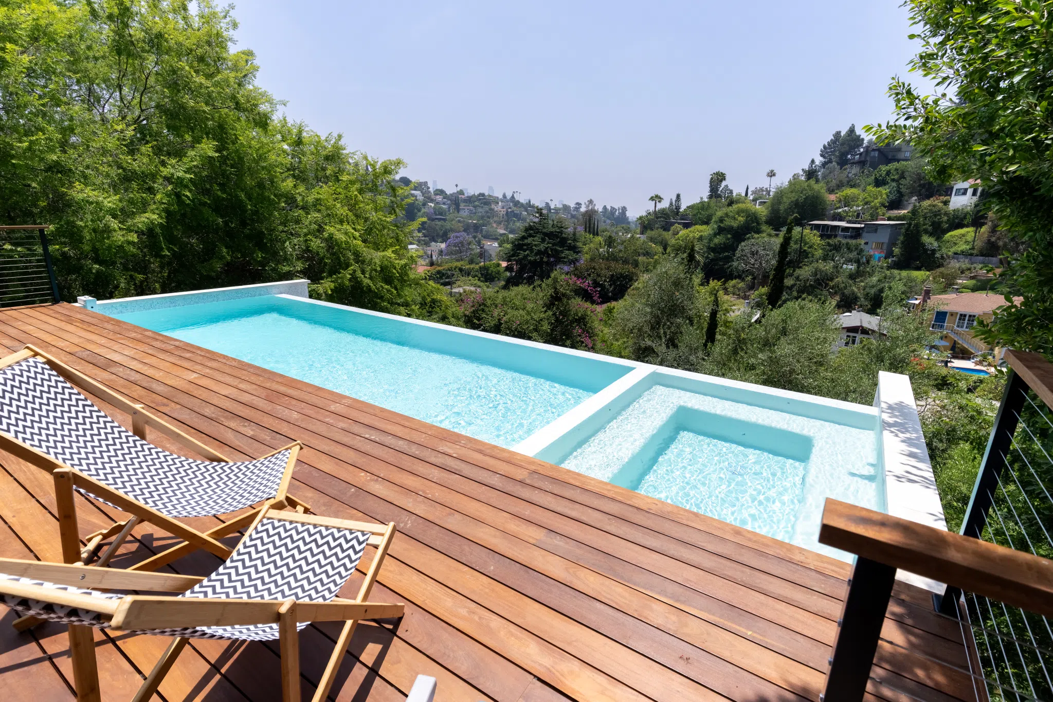 A wooden deck with lawn chairs that extends out to a pool and hot tub. These have a front view of a valley. An example of properly planning a deck